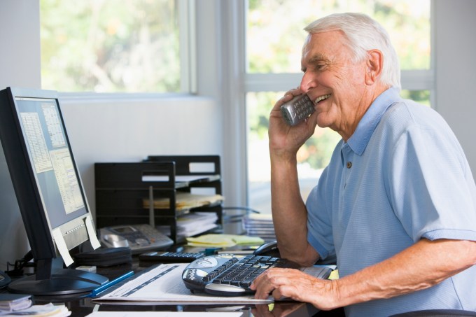 Man in home office on telephone using computer smiling